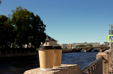 Naklejka premium Two coffee and tea cups standing on stone embankment near the river in the city