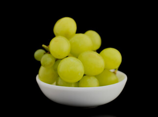 Bunch of sweet juicy grapes with ceramic white utensils, close-up, isolated on black.
