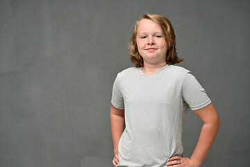 Smiling teenager boy stands right in a gray t-shirt on a gray background