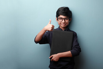 Portrait of a happy boy holding a laptop and showing thumbs up