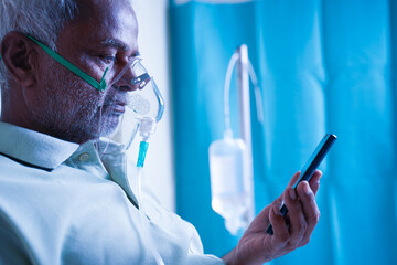 Close up of Sick elderly man with on ventilator Oxygen mask checking health status report on mobile...