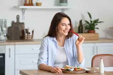 Obraz na płótnie Canvas Beautiful young woman eating tasty quesadilla at home