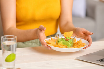 Obraz na płótnie Canvas Young woman eating tasty nachos at home, closeup
