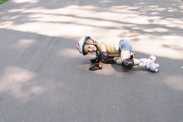 little caucasian girl is rollerblading in the park. the child fell on the asphalt. baby in...