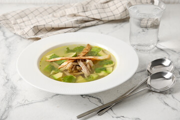 Plate with tasty Sopa de Lima soup and glass of water on light background