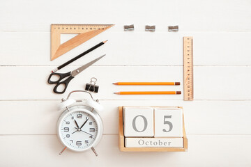 Cube calendar, alarm clock and stationery on white wooden background