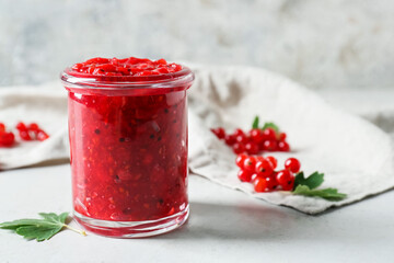 Jar of tasty red currant jam and berries on light background