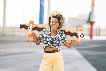 afro woman holds a skateboard with her hands while looking at the camera