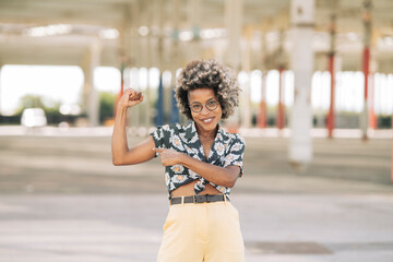 Happy afro woman stands points her arm straining in urban street