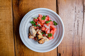 Meat with tomato and pomegranate seeds salad served in a bowl over rustic wooden background.