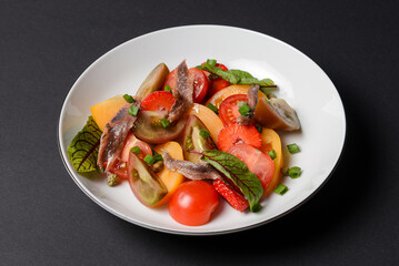 Vegetable salad made of tomatoes and fish slices, served in a white plate over black background.