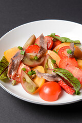 Vegetable salad made of tomatoes and fish slices, served in a white plate over black background.