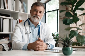 Portrait of handsome mature doctor sitting at desk in modern office.