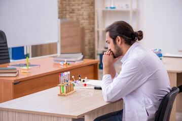 Young male chemist sitting at the desk in the classroom