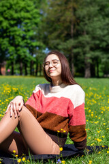 A beautiful young lady sitting on the grass enjoys life, feeling happy and relaxed in the park