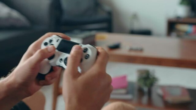 Close-up of the hands of a young man playing video games on a game console in front of a widescreen TV. High quality 4k footage