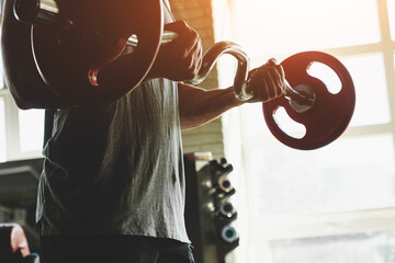 Silhouette photo of a muscular young athlete doing exercises with a barbell in the gym. Power training close up