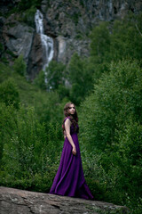Fototapeta premium girl in a purple dress against the background of a mountain waterfall