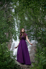 Obraz na płótnie Canvas girl in a purple dress against the background of a mountain waterfall