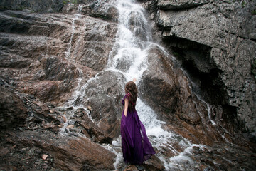 girl in a purple dress against the background of a mountain waterfall