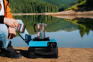 Man preparing coffee on camping stove by the lake