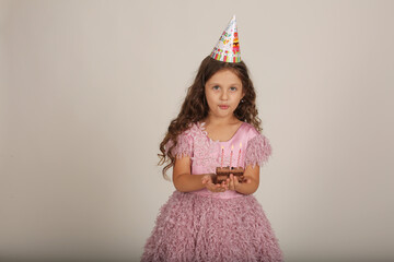 beautiful happy brown-haired girl with curly hair in a pink dress with a piece of cake in her hands birthday