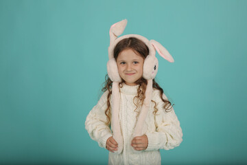 a beautiful happy brown-haired girl with curly hair in a white sweater with pink bunny ears on a blue background