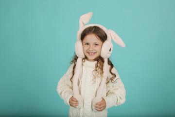 a beautiful happy brown-haired girl with curly hair in a white sweater with pink bunny ears on a blue background