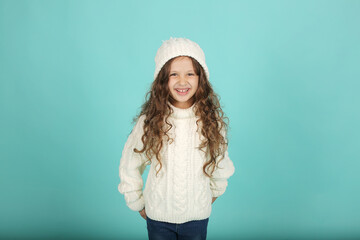 beautiful happy brown-haired girl with curly hair white sweater and winter hat blue background with snow in her hair