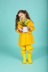 a beautiful brown-haired girl with curly hair in yellow boots, a jacket and trousers with a bucket of flowers on a blue background