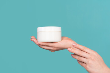Hand cosmetic care. Beautiful womans hands with cosmetic bottle on the blue background. Beautiful woman hands with cream. Proposing a product. Gestures for advertisement.