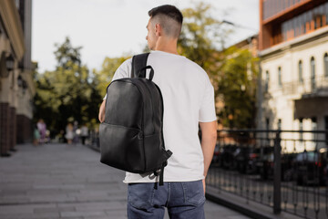 Rear view man walking in city with black leather backpack