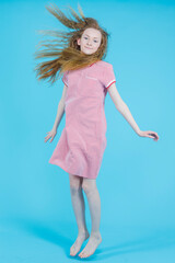 Youth Lifestyle Ideas. Active Teenage Girl In Red Checked Dress Moving in High Jump Against Blue Background.