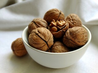 Walnuts in a white bowl on a white linen cloth, one nut is cracked open