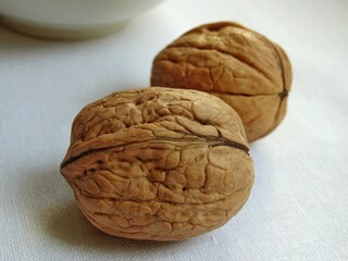 Two whole walnuts on a white linen cloth, closeup