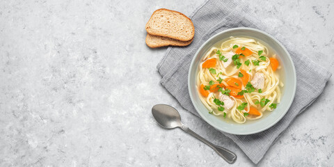 Chicken soup with noodles on a gray concrete background. Top view, flat lay, copy space. Wide composition