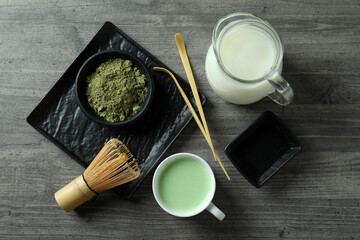 Fototapeta na wymiar Cup of matcha latte and accessories for making on gray textured table