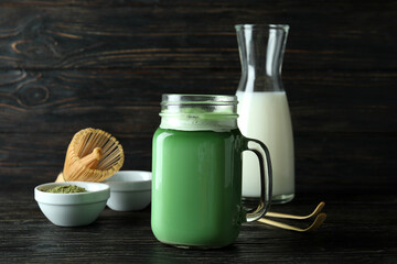 Glass jar of matcha latte and accessories for making on wooden background