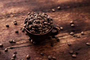 Coffee beans in a clay cup on a brown wooden old background.