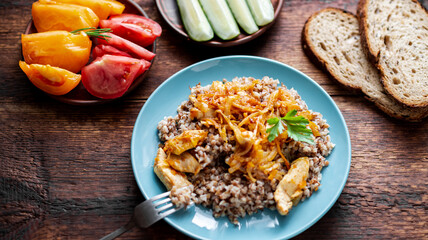 Buckwheat porridge with meat, onions and carrots on a wooden background. With fresh vegetables, cucumbers and tomatoes.