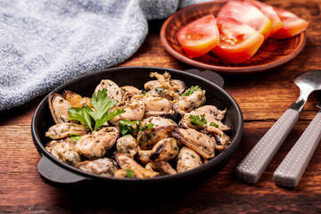 Peeled mussels in sauce on a dark wooden background.
