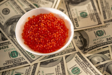 Red caviar in a white plate on 100-dollar bills. The concept of wealth and expensive food.