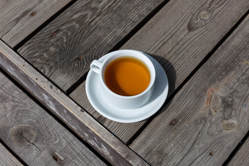 Fototapeta na wymiar a cup of tea in a white mug and saucer on a wooden background on a sunny morning outside