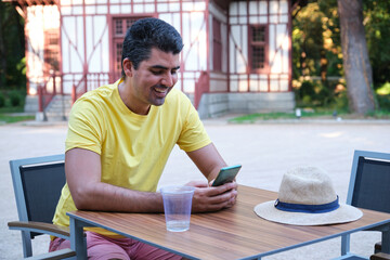 Tourist smiling and using the smartphone sitting on a bar summer terrace.