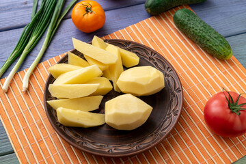 Tubers of raw peeled cut potatoes on a plate on the kitchen table with vegetables. Preparation for cooking.