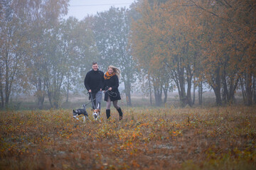 Happy young family couple with two dogs running in autumn park