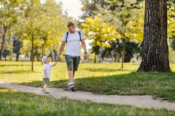 Happy childhood. Father and son walking through the woods on a sunny summer day. Dad holds his...