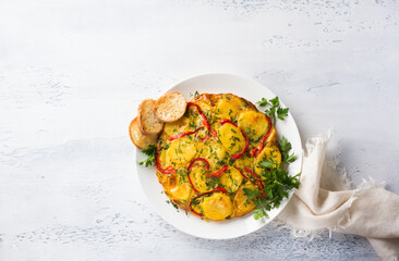 Potato tortilla with bell peppers and herbs on a light gray textured background, top view....
