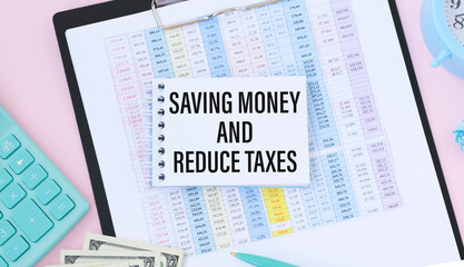 Fototapeta na wymiar Text SAVING MONEY AND REDUCE TAXES on card on office desk with laptop, calculator, chart, clipboard, glasses, pen. Flat lay, top view.