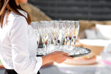 Midsection of waiter offering champagne at poolside.Serving with ice on a tray. Swimming pool party concept.